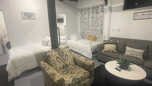 Un dormitorio con dos camas, un sofá, un sillón estampado y una mesita redonda con una planta.
