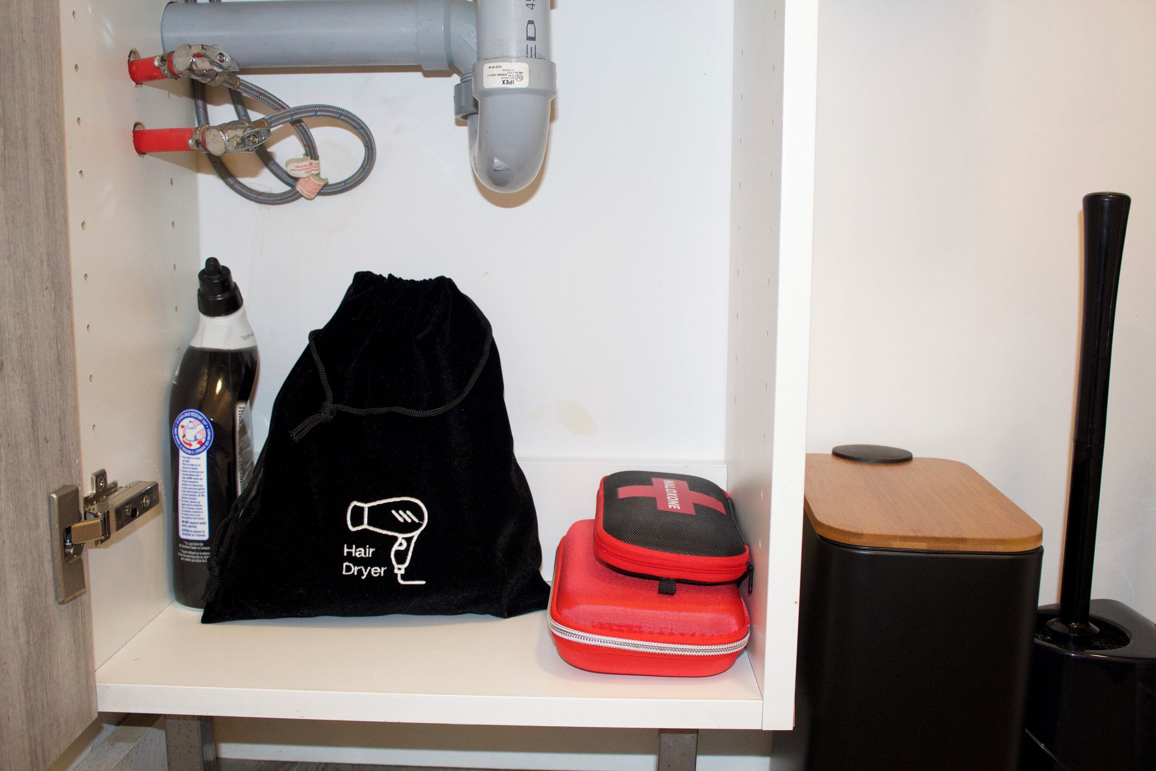 Une salle de bain avec un sèche-cheveux, un sac rouge et un sac noir posés sur une étagère blanche.