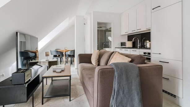A modern living room with a sofa, coffee table, and TV, connected to a kitchen with white cabinets and a dining area with chairs and a table. - Blueground | Sihlfeld, washer/dryer, nr Zürich HB (Zurich)