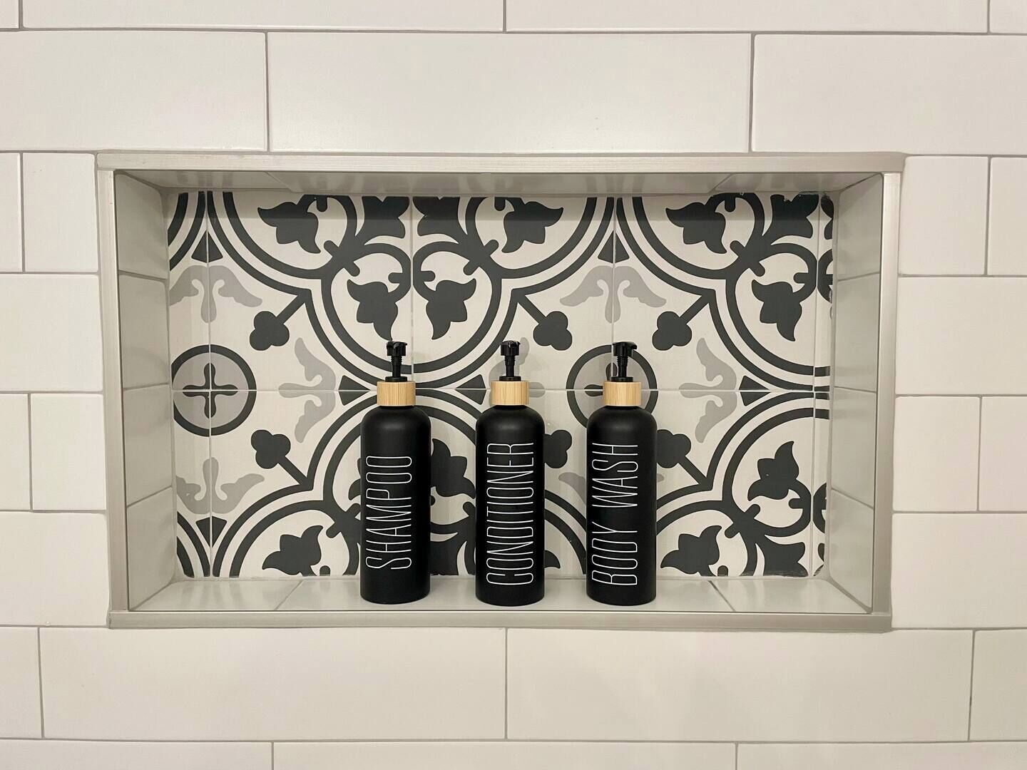 Ein Badezimmerschrank mit drei schwarzen Flaschen, beschriftet mit „SHAMPOO“, „CONDITIONER“ und „BODY WASH“.