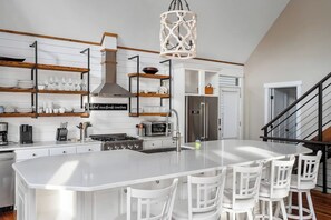 A modern kitchen with white cabinetry, a central island with bar stools, a stainless steel refrigerator, and a hanging light fixture. - Close to Clemson with a beautiful view of Keowee! (Seneca)