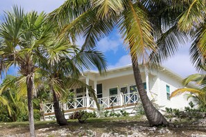 A white house with a balcony, surrounded by palm trees and a clear sky. - A serene 2-bedroom retreat where laid-back island luxury meets tranquil beauty (Great Guana Cay)