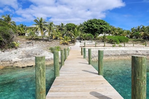 A wooden pier leading to a beach with clear turquoise water, surrounded by palm trees and a white building. - A serene 2-bedroom retreat where laid-back island luxury meets tranquil beauty (Great Guana Cay)