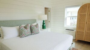 A neatly made bed with white linens and floral-patterned pillows, a bedside table with a green lamp, and a wicker wardrobe. - A serene 2-bedroom retreat where laid-back island luxury meets tranquil beauty (Great Guana Cay)