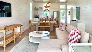 Una sala de estar acogedora con sofá, mesa de centro y mobiliario de mimbre. Hay un comedor con sillas y una mesa, y una cocina al fondo.