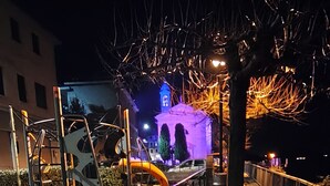 A nighttime outdoor area with a metal fence, a pathway, and a building with illuminated arches in the background. - Romantic house. Veranda with panoramic view. Garden. Barbecue. Parking space (Colonno)