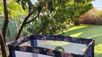 A playpen with a floral pattern, placed on artificial grass, surrounded by trees and a fence.