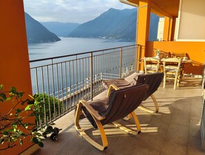 Un balcón con dos sillas, una mesa y vistas a un lago y montañas.