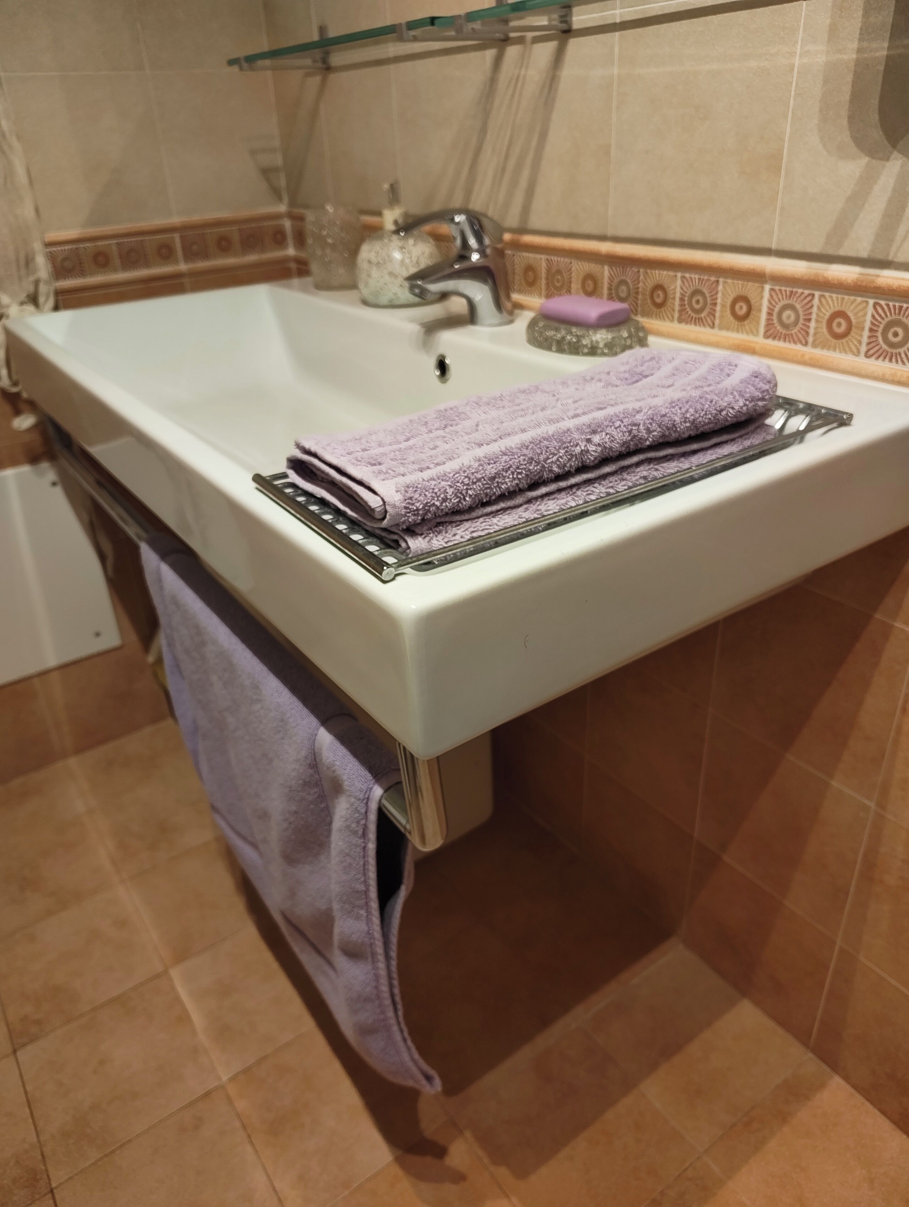 A bathroom with a white sink, a glass shelf above it, and a purple towel on the edge.
