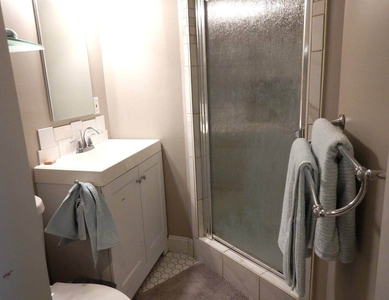 A bathroom with a shower, a sink, and a towel rack.