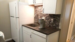 Una cocina compacta con muebles blancos, lavavajillas, refrigerador de doble puerta y salpicadero de azulejos.