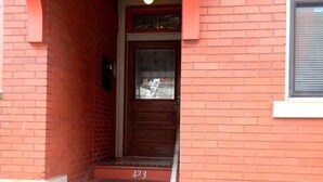 Una escalera conduce a una puerta con el número 423, flanqueada por muros de ladrillo rojo y un techo blanco.
