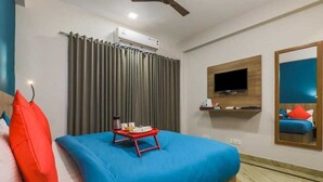 A hotel room with a bed, a TV mounted on the wall, a mirror, and a window with curtains. - Loginn Stays #1 (Gurugram)