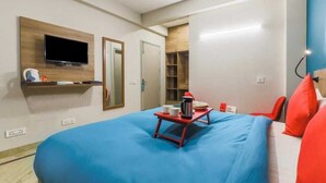 A hotel room with a bed, a television mounted on the wall, a small table with a kettle and cups, and a red chair. - Loginn Stays #1 (Gurugram)