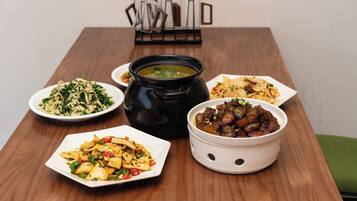 A wooden table with various dishes including a bowl of soup, a plate of noodles, a bowl of meat, and a plate of stir-fried vegetables.