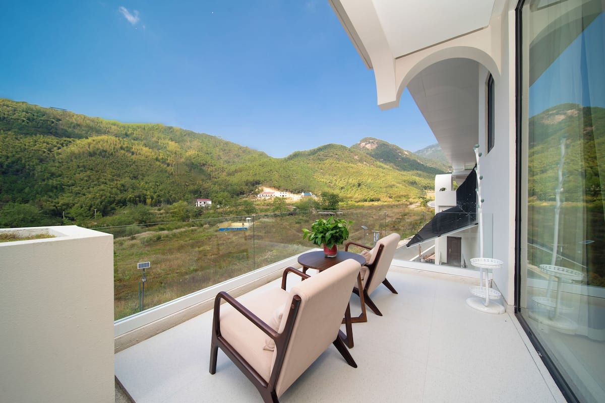 A balcony with a table and chairs, overlooking a mountainous landscape.