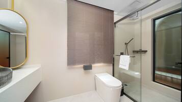 A modern bathroom with a toilet, a glass shower enclosure, and a mirror with a gold frame.