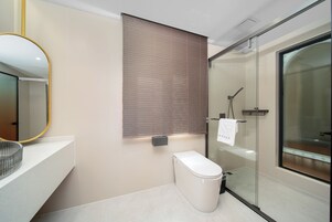 A modern bathroom with a toilet, a glass shower enclosure, and a mirror with a gold frame.
