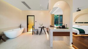 A modern bathroom with a freestanding bathtub, a small round table with a chair, and a bed with a wooden headboard. - Bright Moon Valley Smart Hotel (Anqing)