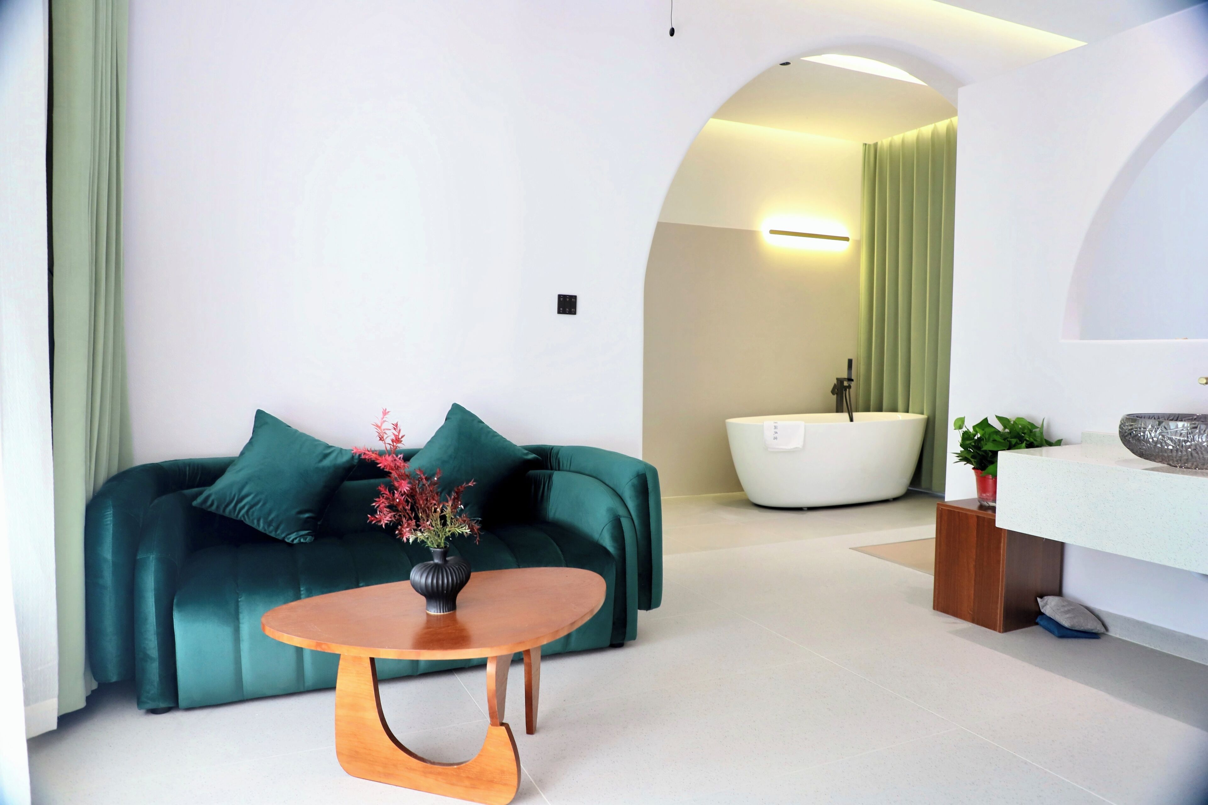 Una sala de estar moderna con un sofá verde, una mesa de centro de madera y una bañera blanca al fondo.