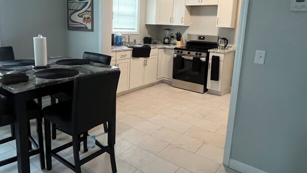 A modern kitchen with white cabinets, a black stove, and a dining area with a marble table and black chairs. - Cozy and comfortable accommodation for six guests. (Dalton)
