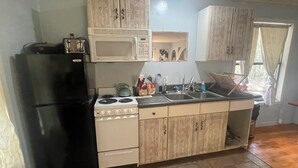 Une cuisine de taille réduite, avec un réfrigérateur noir, une cuisinière blanche, un four à micro-ondes et des armoires en bois.