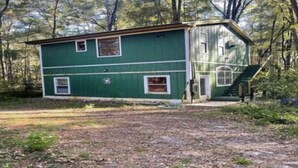 Une maison à deux étages, à l’extérieur vert et aux bordures blanches, entourée d’arbres.