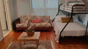 Un espace de vie compact comprenant un canapé, une petite table avec une plante, un lit superposé et un ventilateur de plafond.
