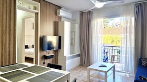 Moderni hotellihuone, jossa on ruokailutila, televisio, kattotuuletin ja parveke, jolta on näkymä.