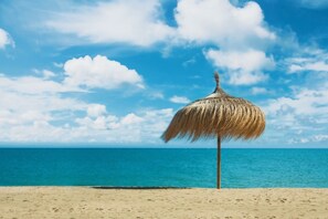 Escena de playa con una sombrilla de paja y cielo azul despejado.