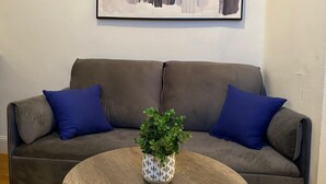 Ein Wohnzimmer mit einem braunen Sofa, zwei blauen Kissen und einem runden Couchtisch mit einem Blumentopf.