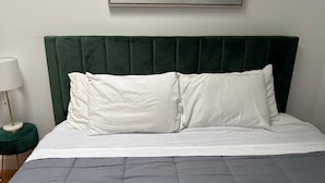 Ein Bett mit einem grünen, gepolsterten Kopfteil, weißen Kissen und einer grauen gesteppten Bettdecke.