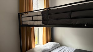 Ein Stockbett mit weißer Bettwäsche, ein Fenster mit Vorhängen und eine sichtbare Steckdose.