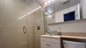 Ein modernes Badezimmer mit Duschabtrennung aus Glas, einem Waschbecken aus Glas und einer Toilette.