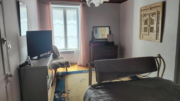 Un dormitorio con una cama, un escritorio con computadora, cómoda, espejo y ventana con cortinas.