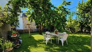 Un patio trasero con una mesa y sillas, una pérgola y diversas plantas en macetas.