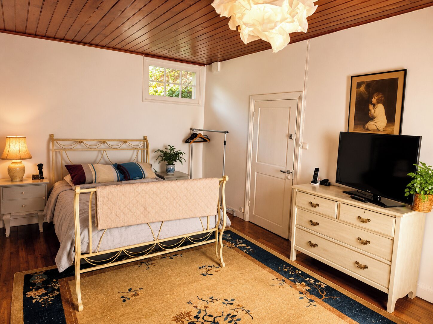 Un dormitorio con cama, mesita de noche, lámpara, televisor, cómoda y ventana.