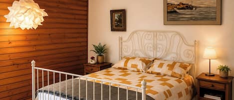 A bedroom with a bed, a nightstand, a lamp, a painting, and a hanging light fixture.