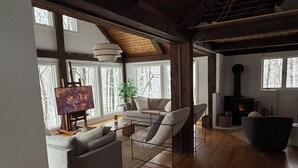 Uma sala de estar ampla, com lareira, janelas grandes e um quadro na parede.