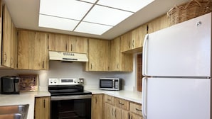 Eine Küche mit Holzausstattung, einem Edelstahlbackofen, einer Mikrowelle und einem weißen Kühlschrank.