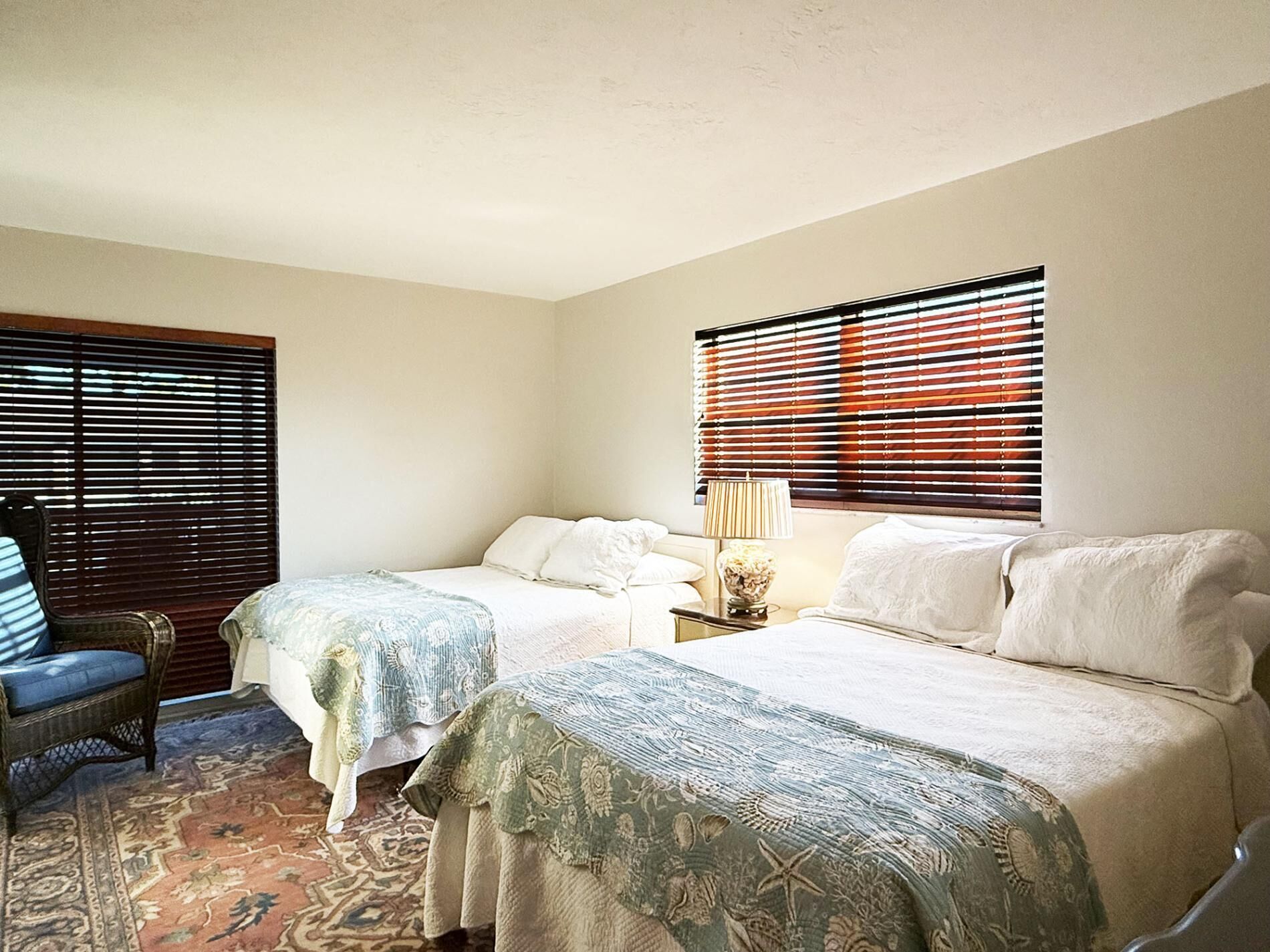 A bedroom with two beds, a chair, and a nightstand with a lamp.