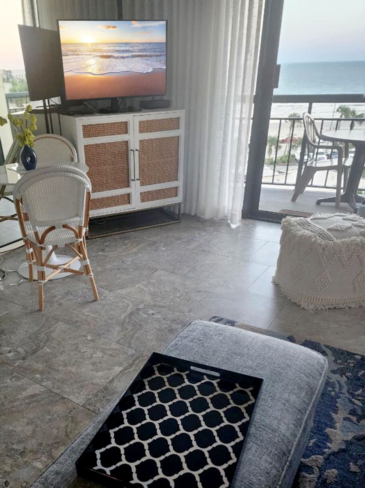 A living room with a TV, wicker furniture, a cushioned bench, and a view of the ocean.