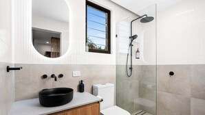 Un bany modern amb un mirall rodó, un lavabo negre, un vàter i una dutxa amb envà.