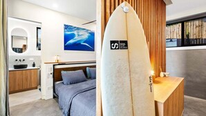 Un dormitori modern amb un llit, un escriptori de fusta i una taula de surf.