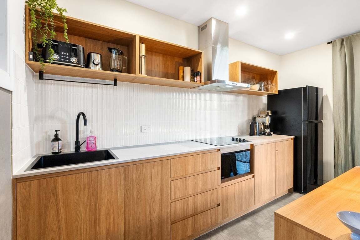 A modern kitchen with wooden cabinets, a black refrigerator, and a built-in oven.
