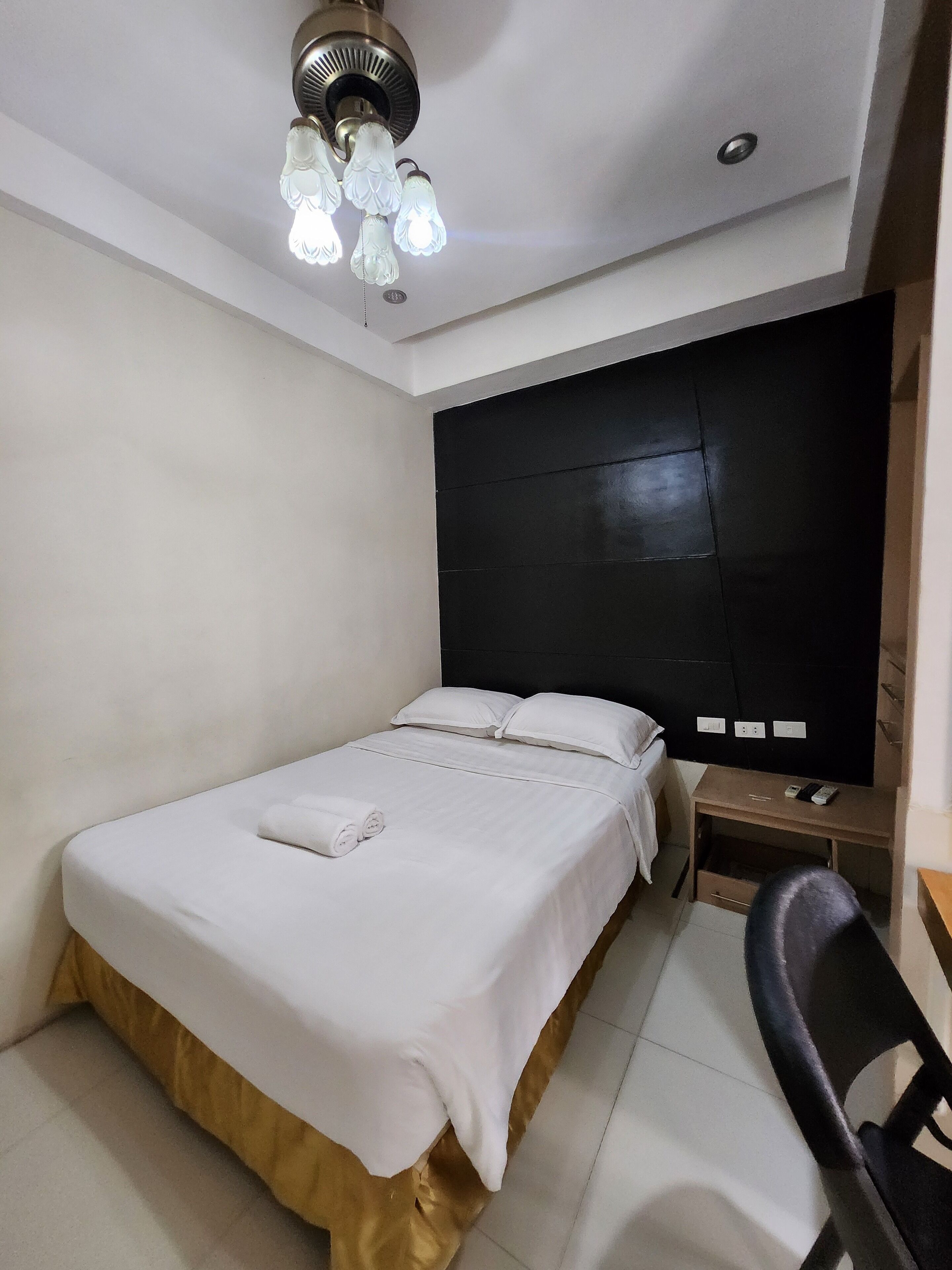 A hotel room with a bed, a desk, a chair, and a ceiling light fixture.