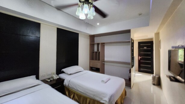 A hotel room with two beds, a ceiling fan, a TV, and a minibar.
