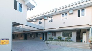 A multi-story building with a covered parking area, a sign warning of slippery conditions when wet, and a small garden area with steps leading to the entrance.