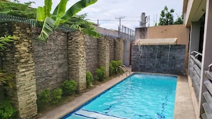 A rectangular swimming pool with a stone wall on one side and a metal fence on the other.