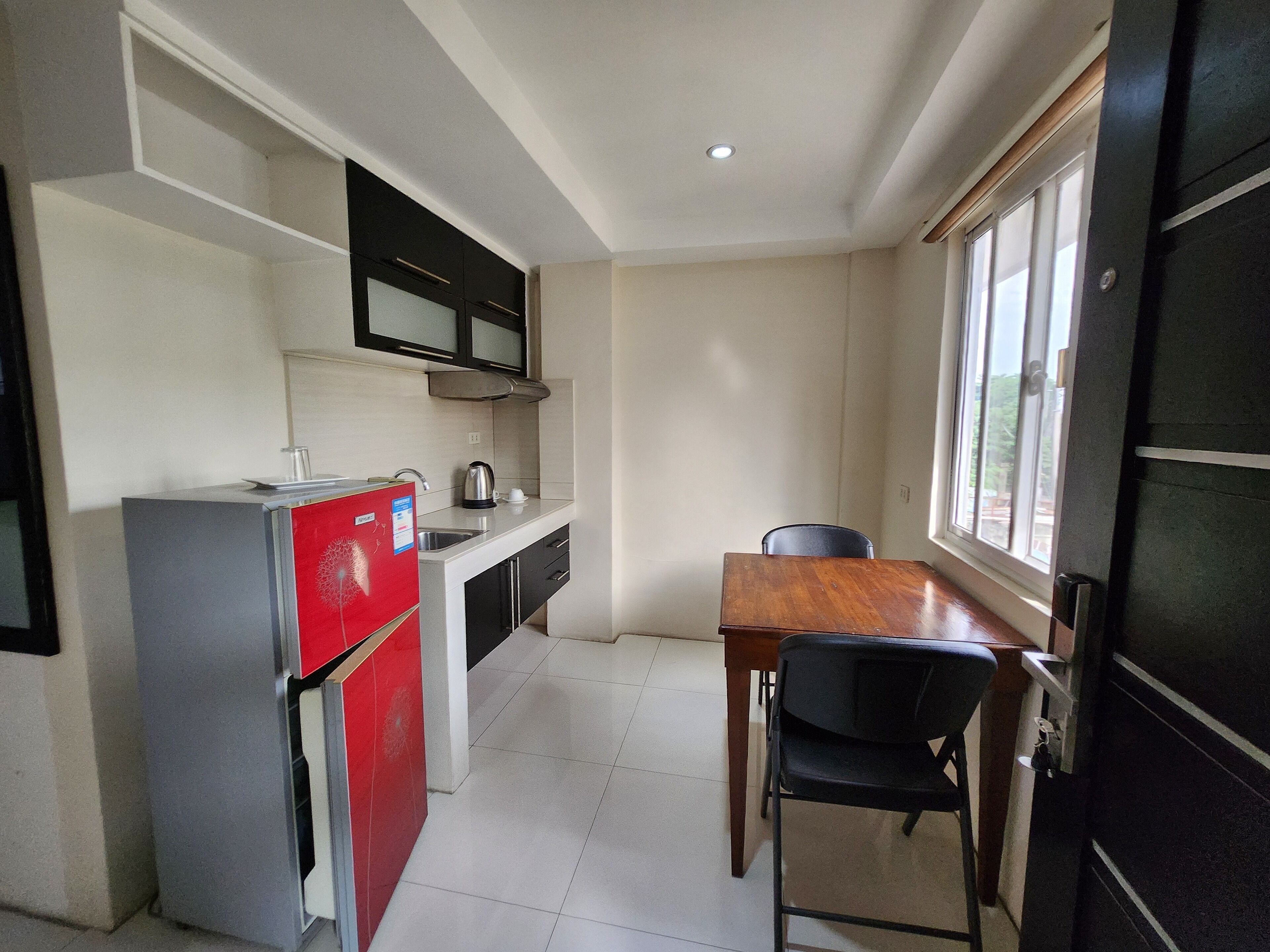 A compact kitchen with a refrigerator, sink, and stove, a dining table with chairs, and a window providing natural light.